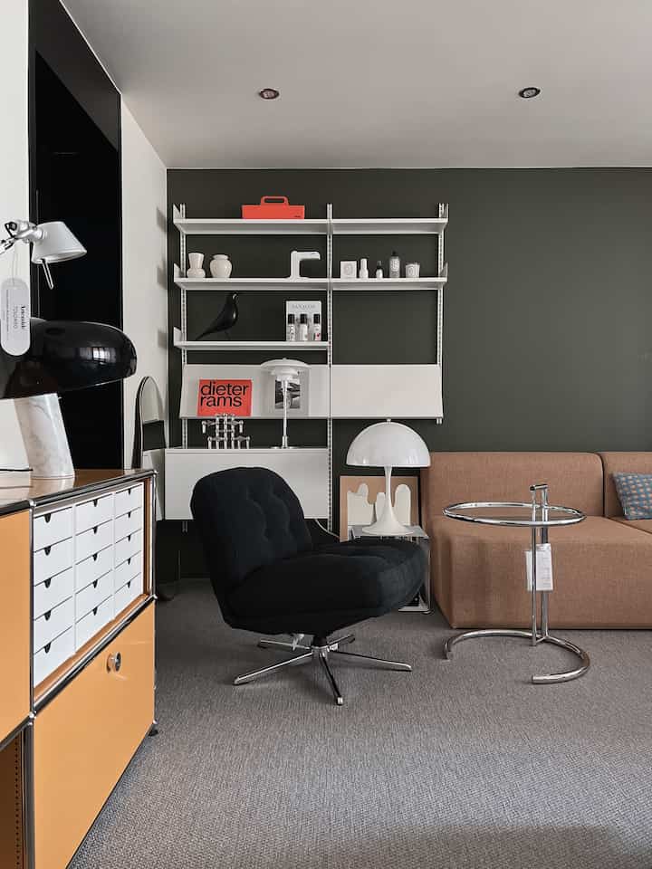 Living room with green walls featuring a brown sofa, black armchair, table lamp, and modular storage in a modern Mid-Century Modern style