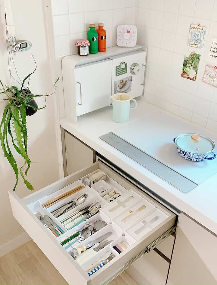 A clean white and natural tone kitchen featuring an organized cutlery drawer and a sleek induction cooktop, creating a cozy atmosphere