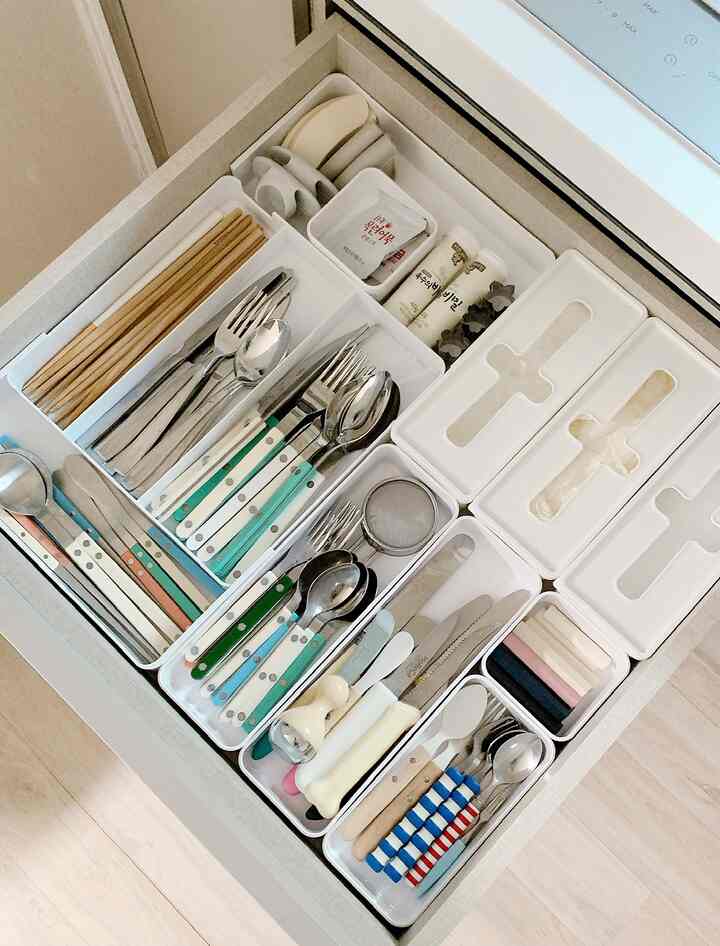 Neatly organized kitchen drawer with various cutlery arranged in white trays creating a tidy storage space