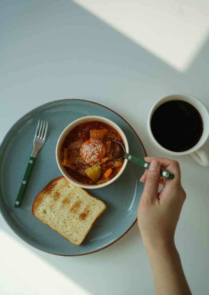 白いテーブルの上にブラウンのトーストとトマトスープが入ったブルーの皿、コーヒーが置かれた雰囲気のあるダイニング