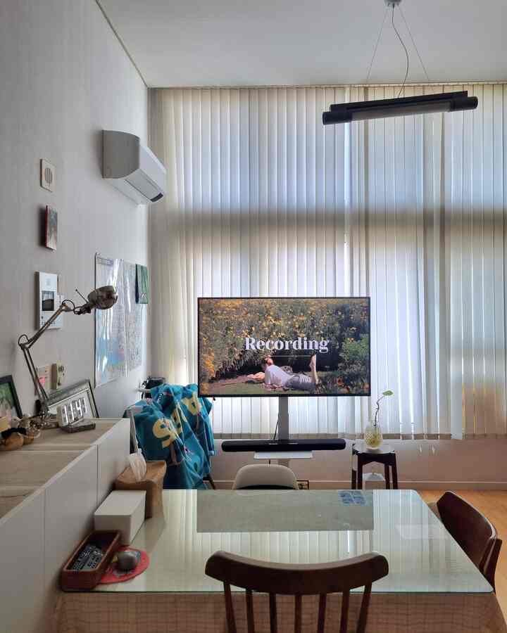 ホワイトとブラウンの色調が特徴のダイニング、巨大なブラインドとテレビスタンドが配置されたシンプルな空間