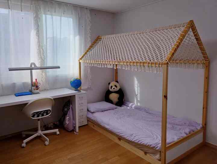 白い壁とカーテン、ナチュラルな木製ベッドと机が配置された、雰囲気のある子ども部屋のインテリア