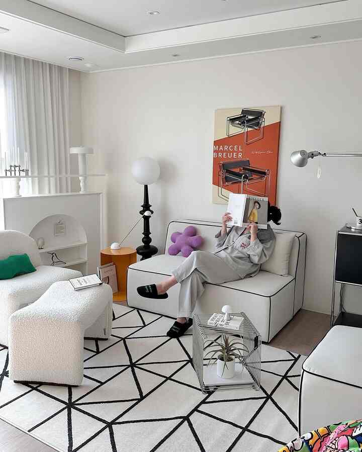 ホワイトとブラックの色調のリビング、モダンなソファとアームチェア、幾何学模様のラグとフロアランプが配置された雰囲気のあるインテリア