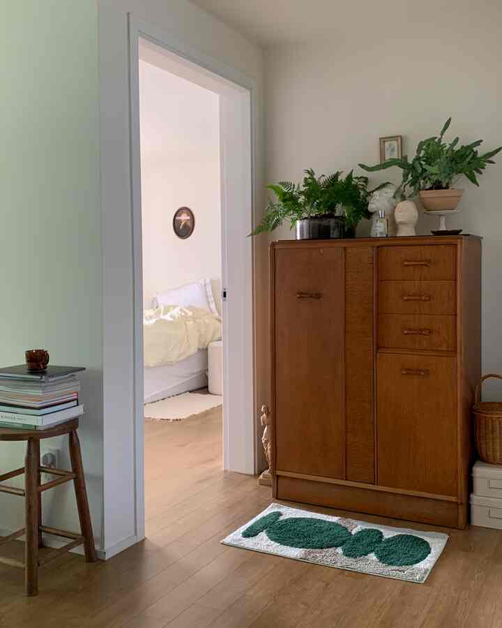 ナチュラルなブラウンとホワイトのトーンの寝室横の廊下、木製のキャビネットや植物、彫刻が配置された居心地の良い空間