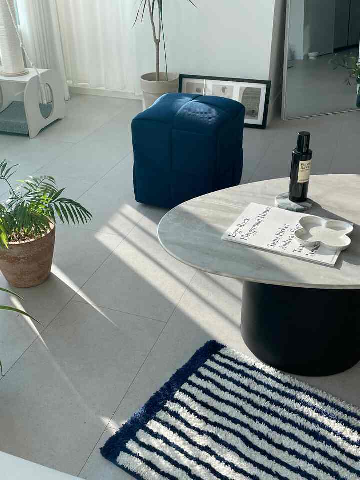 Navy and white toned living room featuring a marble coffee table, navy stool, plants, and striped rug, creating a bright modern space