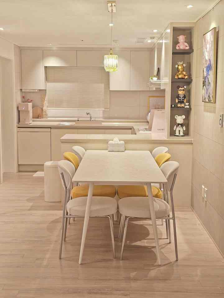 白とベージュの木目調が調和したナチュラルなダイニングルーム。モダンなキッチンスペースにテーブルと椅子が配置された明るい空間