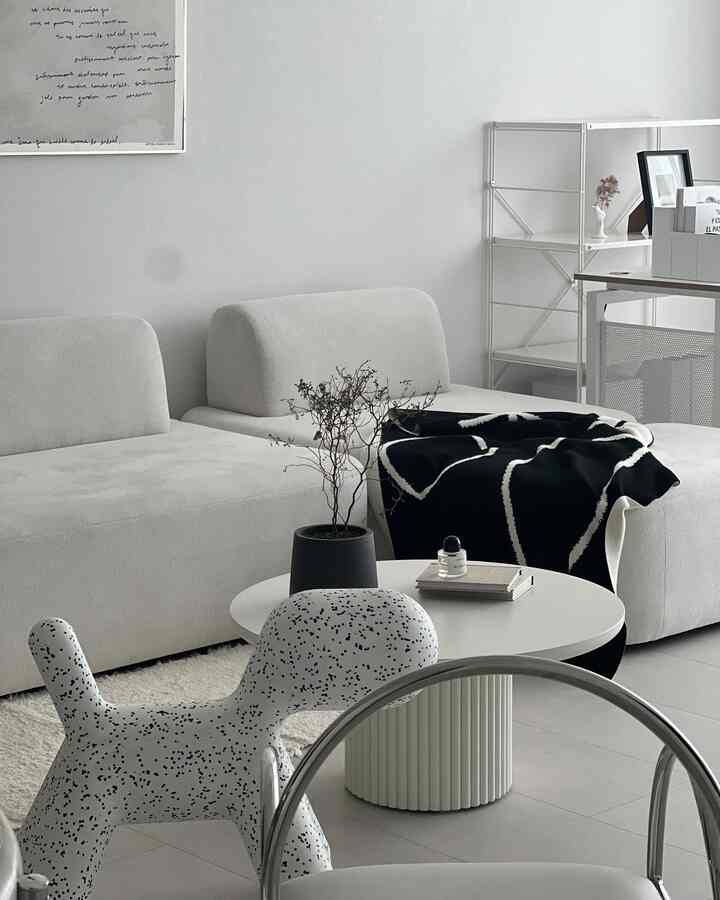 Black and white toned living room featuring simple sofas, round coffee table, and dog-shaped chair in a modern minimalist setting