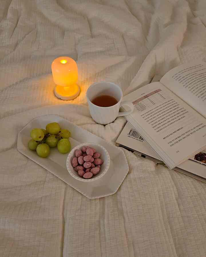白い寝具の上にキャンドルライト、カップ、皿、開いた本が置かれた雰囲気のある寝室