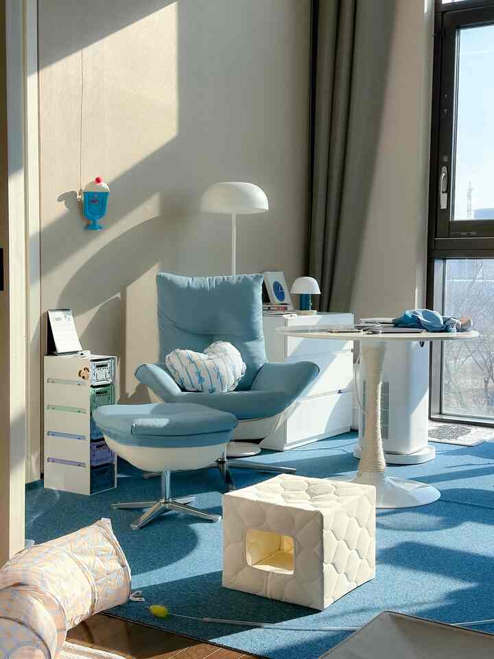 Soft blue and white toned living room featuring a comfortable armchair, dining table, and cat hideout and tunnel creating a cozy atmosphere