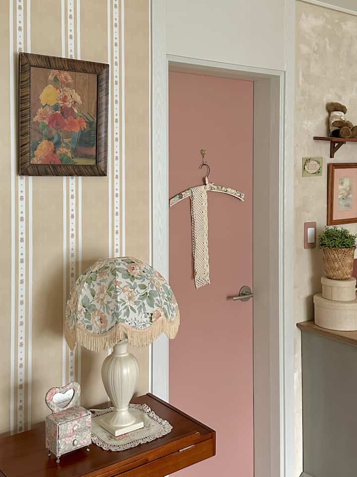 ベージュとピンクの壁紙とドア、花柄のテーブルランプと額縁が配置されたヴィンテージ風の空間