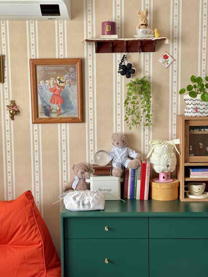A vintage-inspired room with beige striped wallpaper backdrop, green plants, orange sofa, framed art, and plush toys arranged for a cozy atmosphere