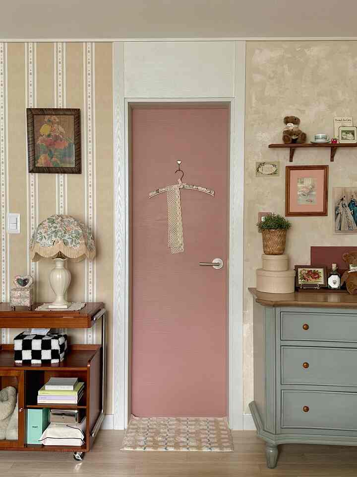 ベージュとピンクのトーンでまとめられた温かみのある空間、ヴィンテージスタイルの家具、壁紙、額縁、棚が印象的に配置されたインテリア