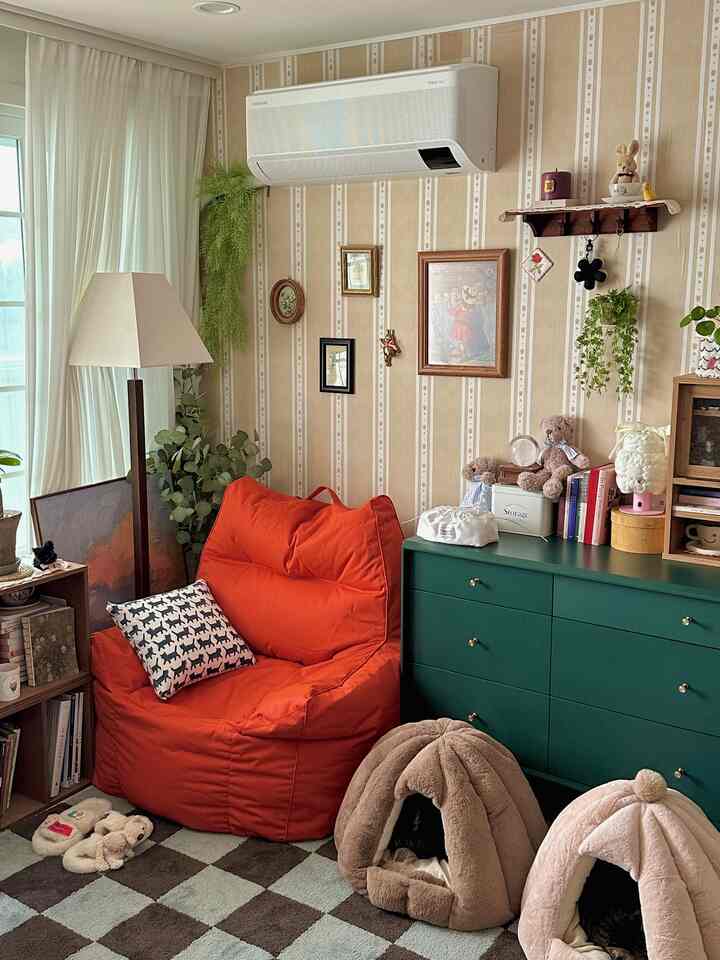Beige wallpapered living room with green dresser, orange bean bag, and pet beds creating a cozy atmosphere