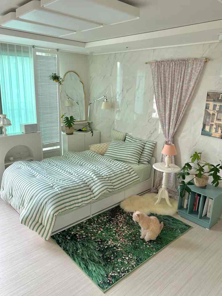 ミント色のストライプ寝具と植物、猫がいる明るい寝室のインテリア