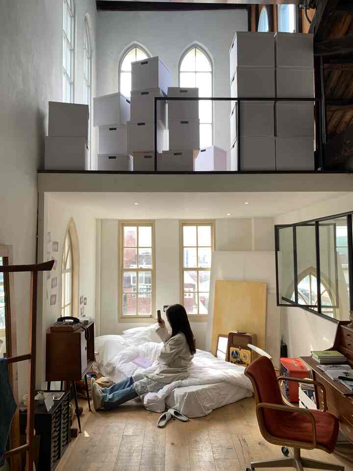 白と木目調のモダンな雰囲気の寝室兼ホームオフィス、ロフトに収納箱が積まれている