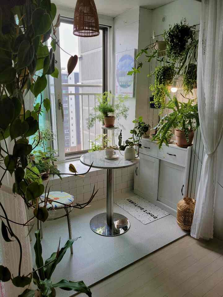白いタイルの床とキャビネット、緑の植物が豊富に配置された小さなホームカフェのバルコニー