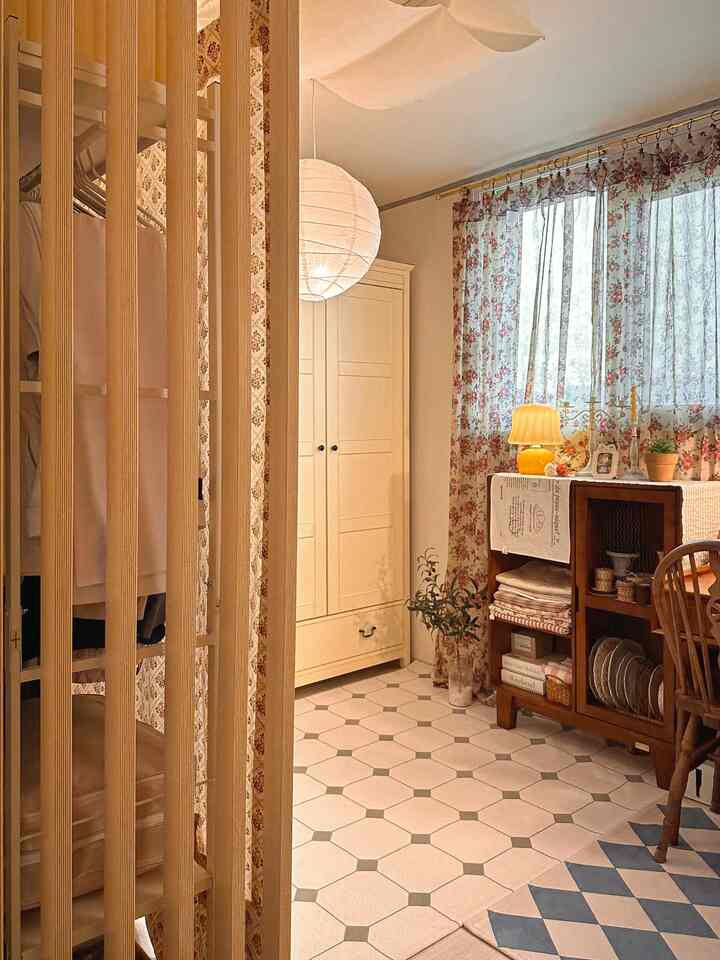 暖かい木目調と明るいクリーム色の家具が配置されたウォークインクローゼット兼小さな部屋、花柄カーテンと木製のパーティションで空間を仕切ったヴィンテージ風のインテリア