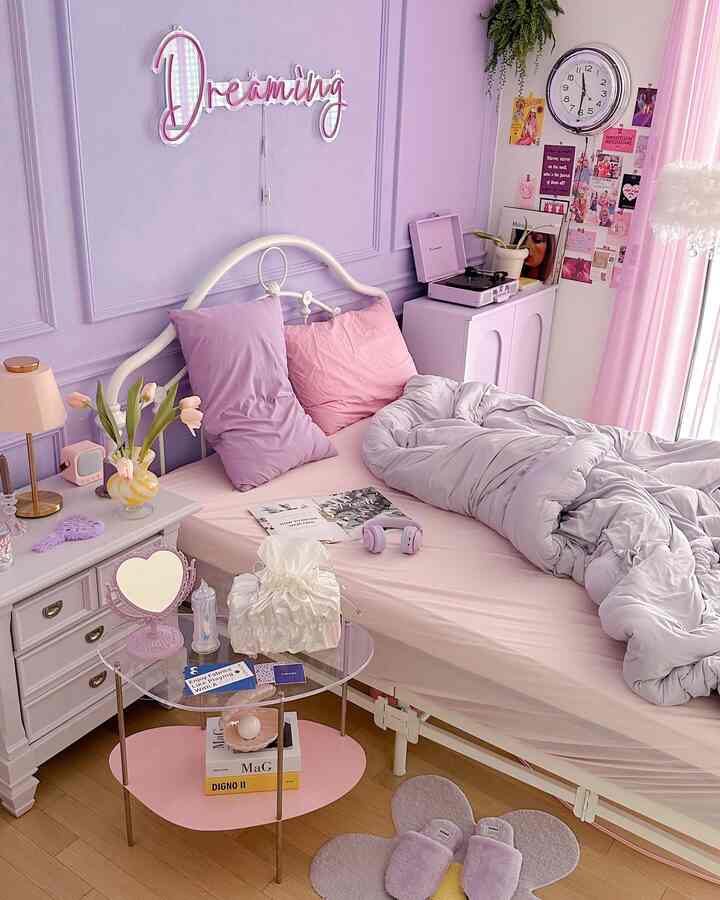 ラベンダーカラーの壁とピンクの寝具が調和した寝室で、化粧台とカーテンが配置された雰囲気のあるインテリア
