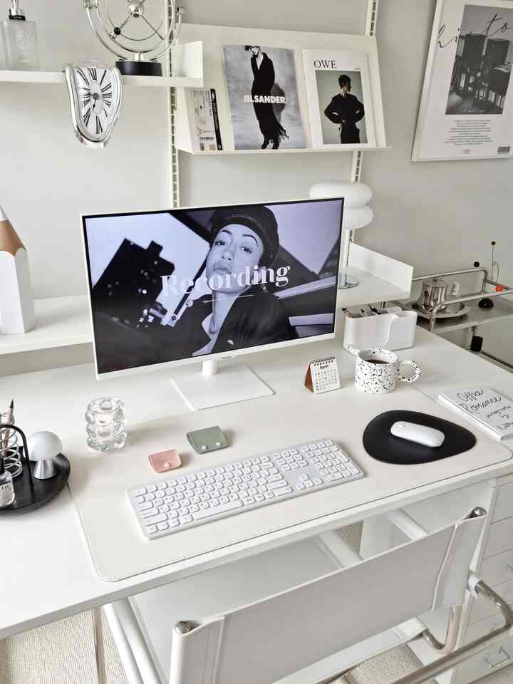 白を基調としたホームオフィス、ホワイトデスクとミッドセンチュリーモダンの時計、モニター、デスクランプが配置された清潔感のある作業空間