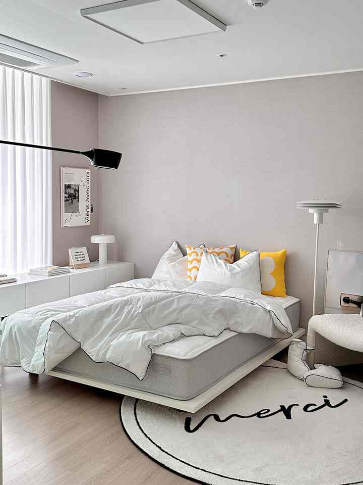 明るい白とライトブラウンのトーンのシンプルモダンな寝室、中央に低いベッドとラグ、左側にテーブルランプが配置された雰囲気のあるインテリア