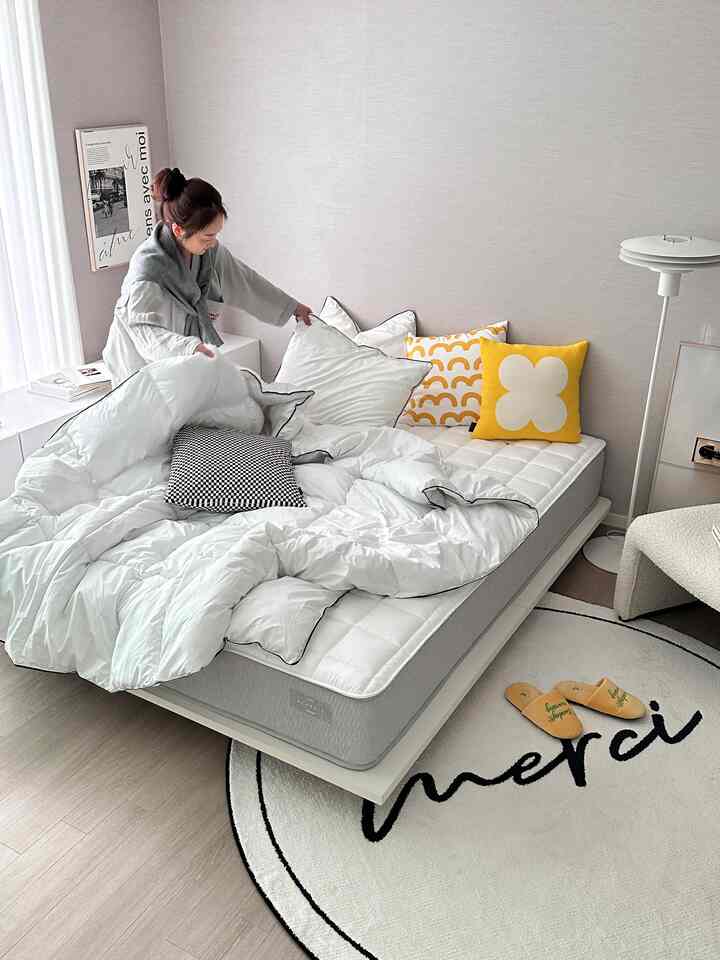 White and yellow toned bedroom space featuring a modern bed, cushions, floor lamp, and circular rug creating a cozy atmosphere