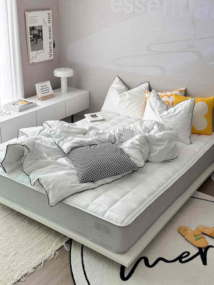 White and yellow toned bedroom featuring a centrally placed bed with cushions in a clean, modern setting