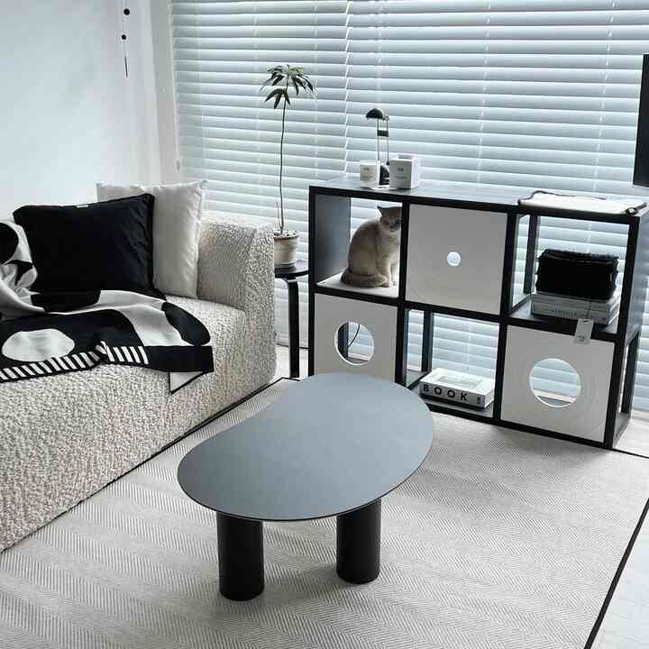 A modern, simple living room in white and black tones featuring a textured sofa, coffee table, and a cat sitting in the cat tower.