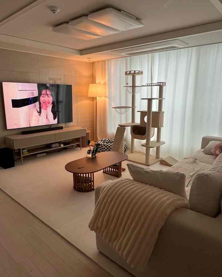 柔らかなアイボリーとベージュの色調のリビング、 大きなソファとキャットタワー、テレビ台が配置された落ち着いた空間