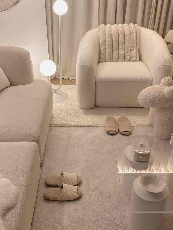 ベージュの色調のリビングルーム、柔らかなブークレのソファとアームチェア、透明なアクリルコーヒーテーブルが配置されたナチュラルモダンなインテリア