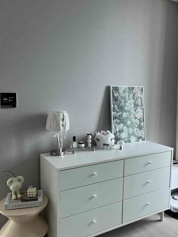 柔らかなグレーの壁を背景に、ホワイトのドレッサーとテーブルランプが配置されたシンプルで清潔感のあるインテリア