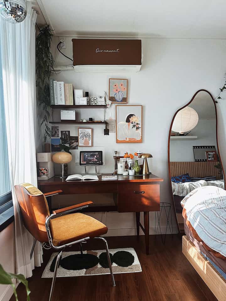 Natural wood tones and white walls blend in a single household study featuring a wooden desk, chair, and large wall mirror creating a cozy reading and work corner