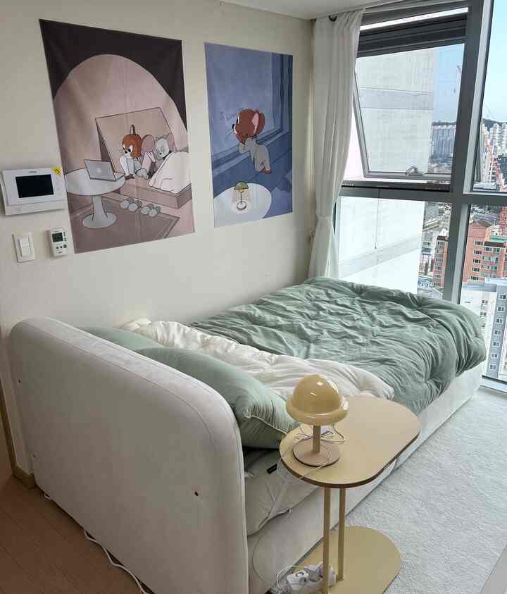 白い壁とカーテンがある一人暮らしの寝室、緑の寝具とサイドテーブルが配置されたナチュラルモダンな雰囲気のインテリア