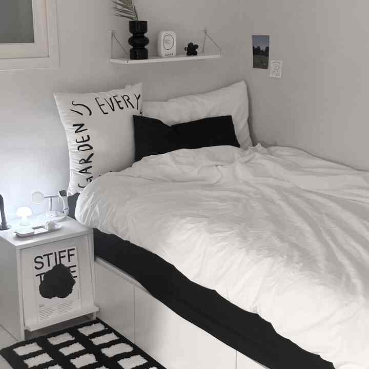 Monotone bedroom in white and black featuring bed, nightstand, lettering cushion, and neat storage design
