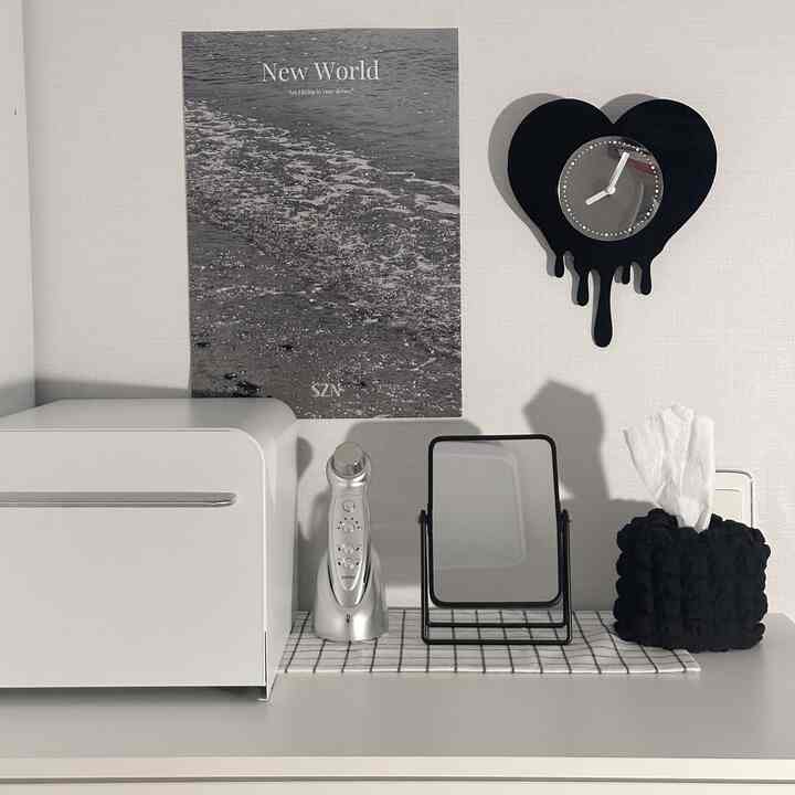 Monotone powder room space with white walls and table featuring a black heart-shaped clock, rectangular mirror, and tissue box