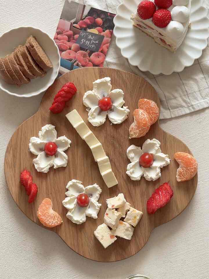 A cozy home cafe space with wood tone and white hues, featuring a wooden serving tray with cheese and fruit as the focal brunch setup