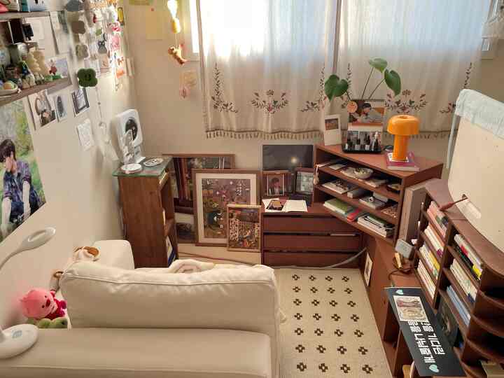 ホワイトのソファとブラウンの木製家具が配置されたコンパクトなリビング、壁に掛けられた複数の額縁や収納家具が印象的なインテリア