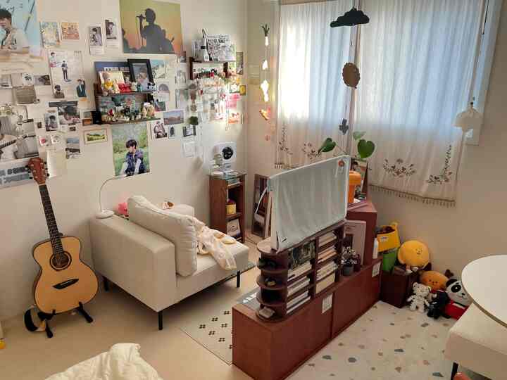 ホワイトとブラウンの色調のリビング、壁にポスターとディスプレイがあり、コンパクトなソファと本棚が配置された雰囲気ある空間