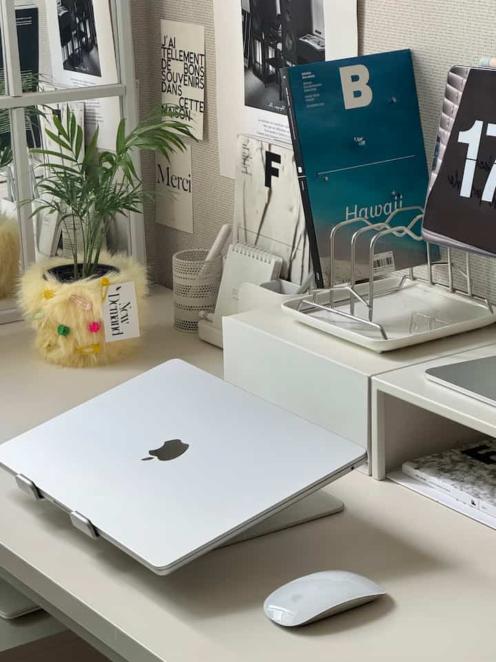 White and silver toned study interior featuring a MacBook with laptop stand on a neat desk setup
