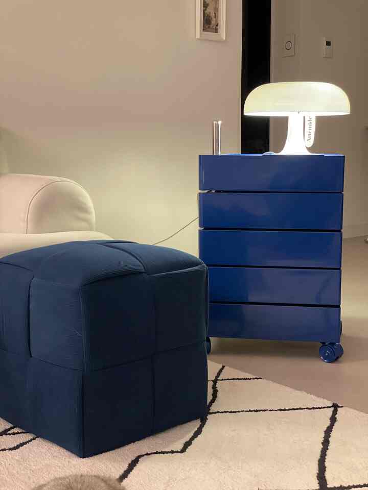 Natural modern living room with white walls, navy stool, blue BINGEURI drawer trolley, and a glowing table lamp