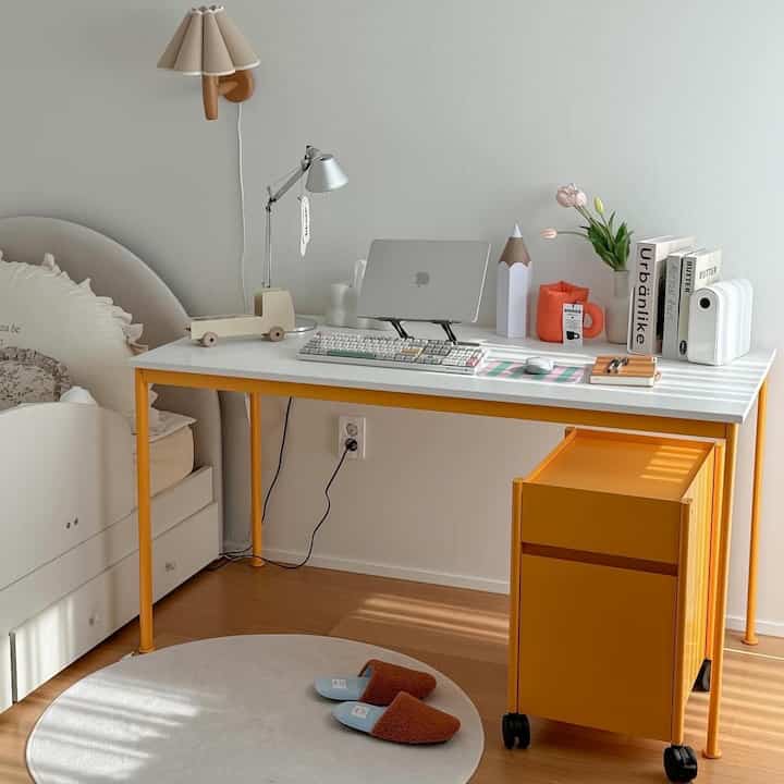 Yellow and white toned study room featuring a simple modern desk with laptop and keyboard, complemented by a matching trolley