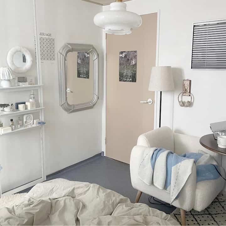 白とベージュの色調の小さなワンルーム、居心地の良いアームチェアと壁棚が配置されたシンプルで自然な雰囲気の寝室