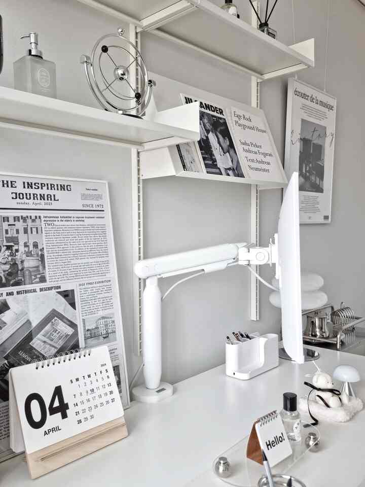 White-toned home office space featuring a neat desk with a monitor arm and decorative objets on shelves creating a simple modern interior