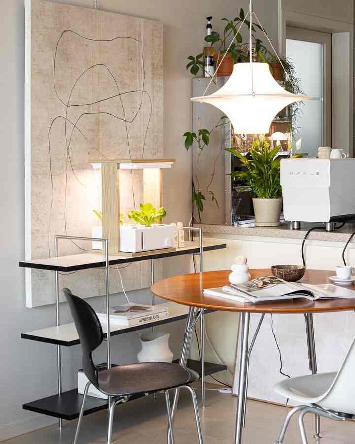 Natural brown-toned kitchen featuring a round wooden dining table, black metal shelving with plants, and a mid-century modern pendant light, creating a cozy atmosphere