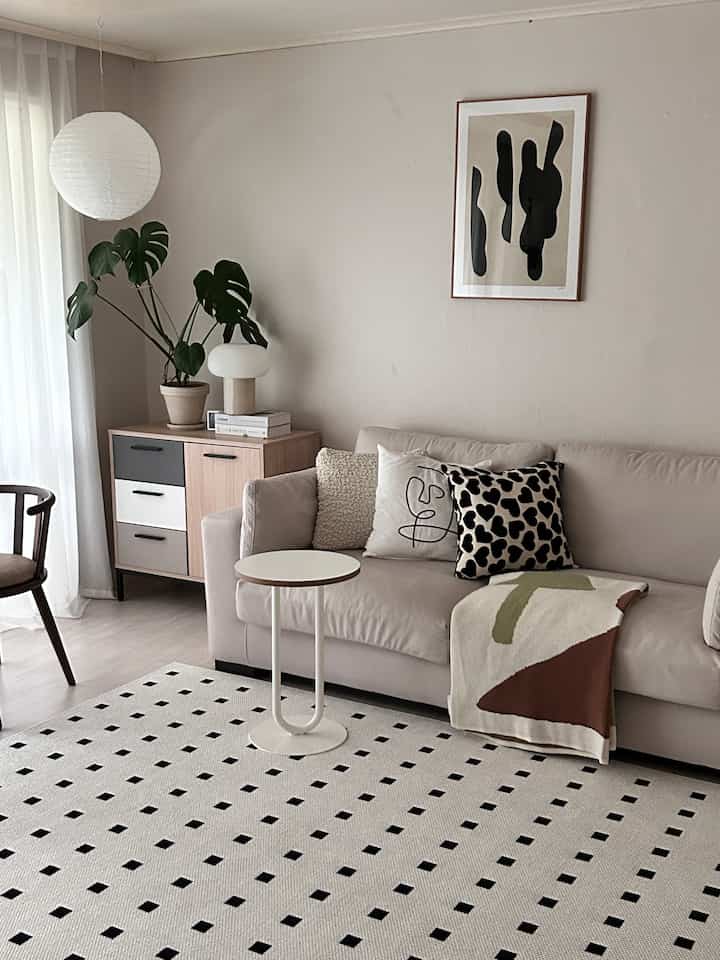 Beige and wood tone living room featuring a sofa with cushions and a throw, plant, and side table in a simple natural setting