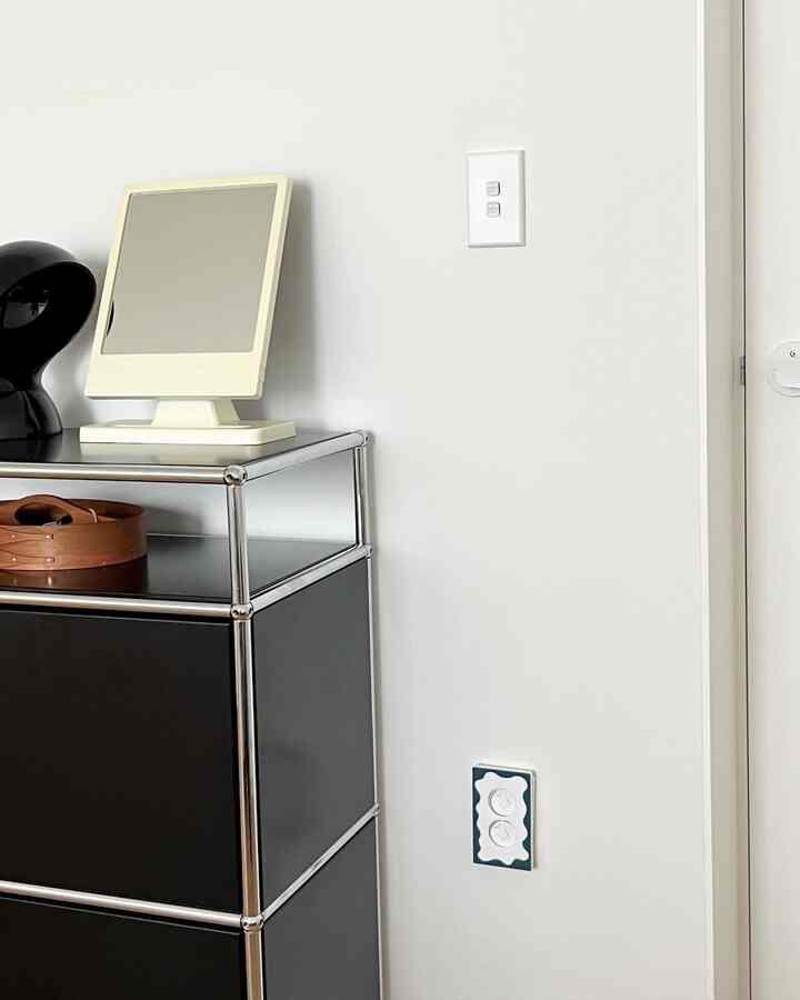 Modern entrance space featuring white walls and door as background, with a black metal-frame cabinet and a table lamp on top