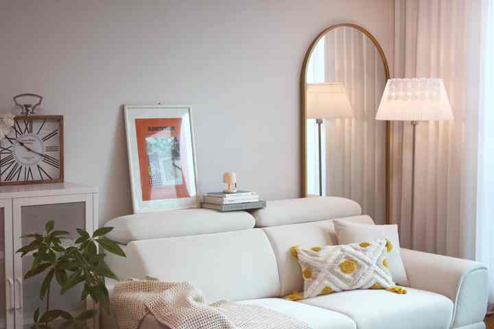 柔らかいアイボリーの色調のリビング、3人掛けソファとアーチ型の全身鏡、フロアランプが配置された落ち着いた空間