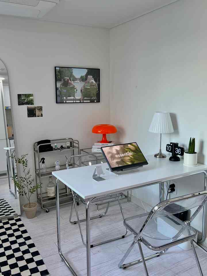 Bright white-toned studio workspace featuring modular furniture, transparent chair, and orange mid-century modern table lamp with clean design
