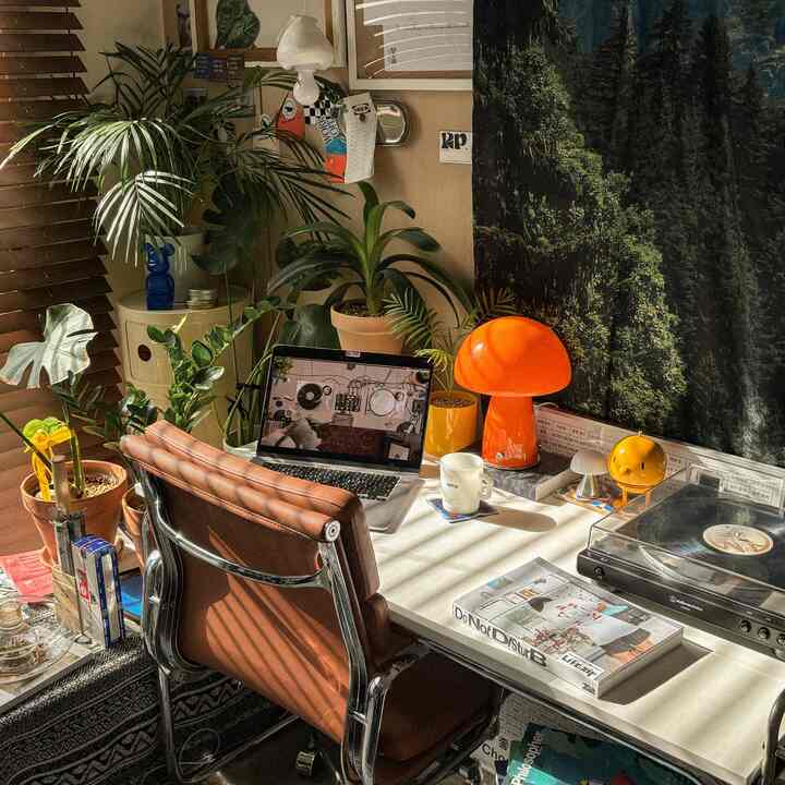 ホワイトのデスクとブラウンのレザーオフィスチェアが配置され、緑の植物とオレンジのマッシュルームランプが調和するミッドセンチュリーモダンなホームオフィス