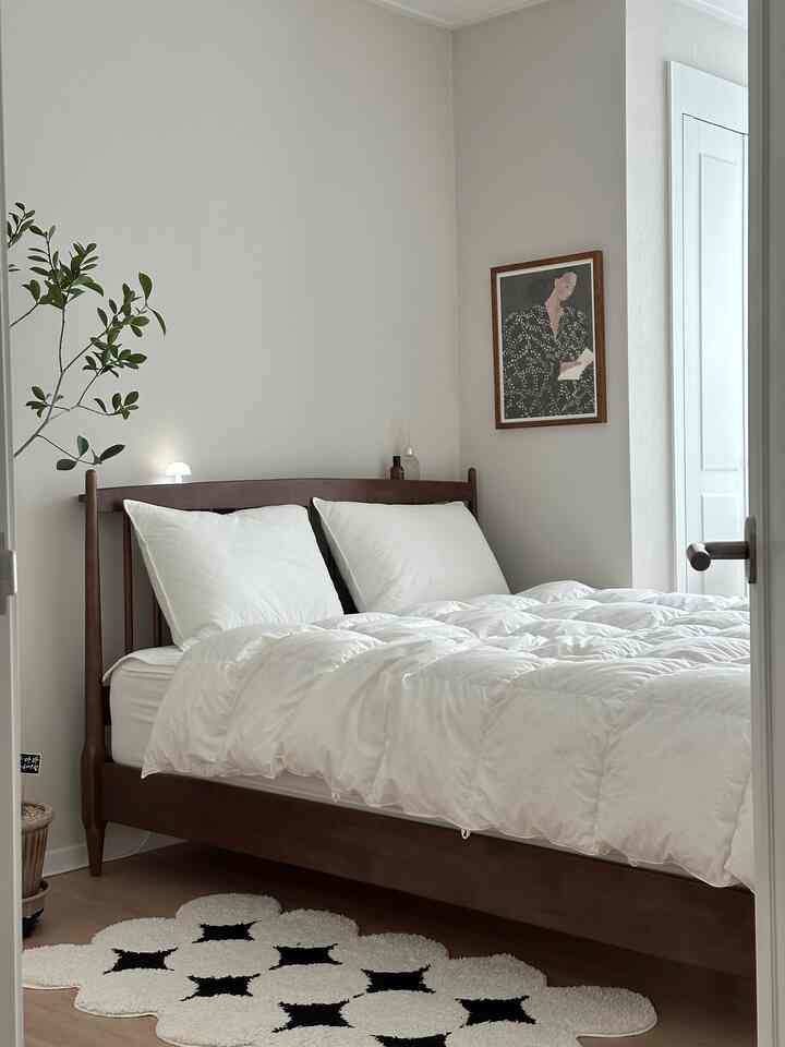 A natural and modern bedroom in wood tones and white, featuring a simple bed and rug with a clean atmosphere