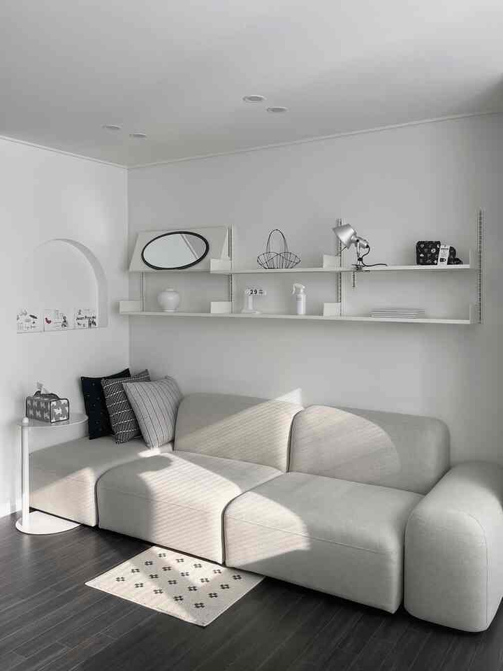 Modern living room with white walls and beige sofa, featuring clean shelves and cushions for a cozy atmosphere
